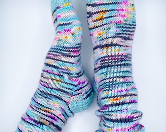 May include: A pair of hand-knitted socks with a light blue cuff and toe. The socks feature horizontal stripes in various colors, including pink, purple, yellow, and gray. The socks are made of soft yarn and are designed to keep feet warm.