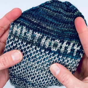May include: Close-up of a knitted sock with a blue and white pattern. The sock is held in a hand, showing the intricate details of the knit.