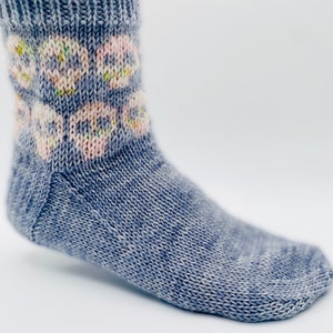 May include: A pair of blue knitted socks with a white and pink floral pattern on the cuff.
