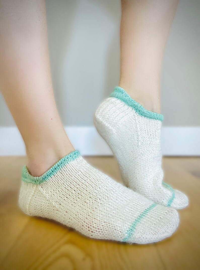 May include: A pair of white ankle socks with a light blue trim. The socks are made of a soft, knitted fabric.