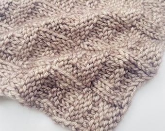 Può includere: Primo piano di un tessuto a maglia beige con un motivo testurizzato. Il tessuto è morbido e ha una lucentezza sottile.