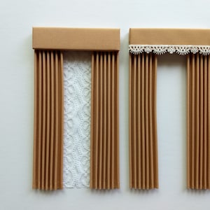 May include: Two miniature brown paper curtains with a white lace curtain in the center. One has a simple brown header, and the other has a white lace trim. The curtains are a decorative element.
