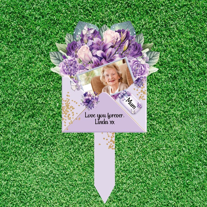 May include: A commemorative garden stake featuring a light purple envelope design adorned with purple and white floral illustrations. A rectangular photo of an older woman is centered, with a small tag labeled Mum and the text Love you forever. Linda xx.