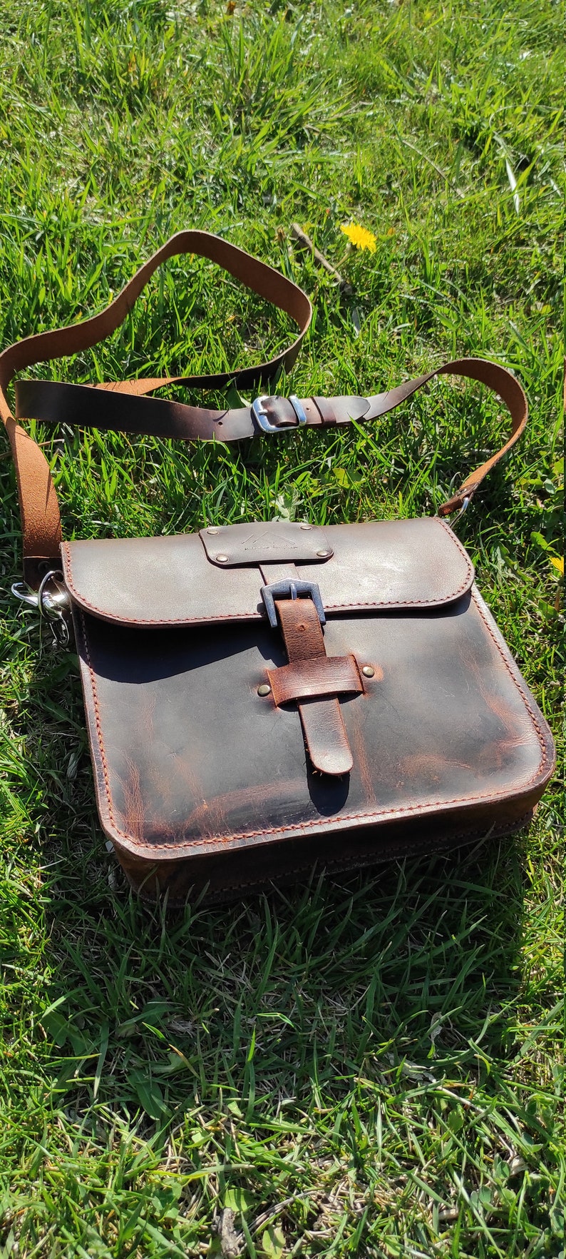 May include: A brown leather messenger bag with a buckle closure and a long adjustable strap. The bag has a distressed look and is made of high-quality leather.