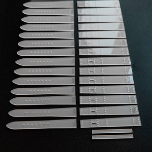 May include: A set of 18 clear plastic watch strap templates, ranging in size from 17/14 to 22/20 mm. The templates are marked with the size in millimetres.