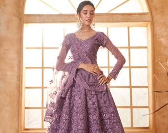 May include: A lavender-colored formal gown with intricate floral embroidery and sparkling embellishments. The dress features a V-neckline, long sleeves, and a flowing skirt. A matching sheer shawl is draped over the shoulder. The gown is suitable for special occasions.