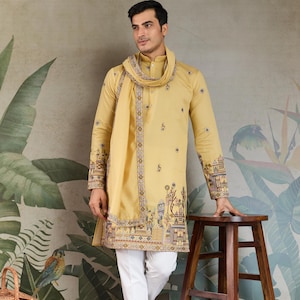 May include: A mustard yellow kurta and matching scarf set with intricate embroidery on the sleeves and hem. The kurta is paired with white pants. The outfit is worn with brown sandals. The background features a botanical mural.