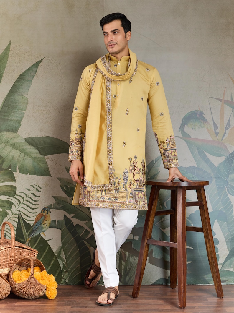 May include: A mustard yellow kurta and matching scarf set with intricate embroidery on the sleeves and hem. The kurta is paired with white pants. The outfit is worn with brown sandals. The background features a botanical mural.