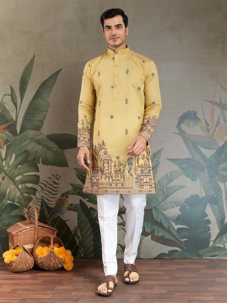 May include: A mustard yellow kurta with intricate embroidery on the cuffs and hem, paired with white trousers. The kurta features a mandarin collar and button-down front. The design includes floral and architectural motifs. The outfit is suitable for festive occasions.