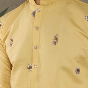 May include: A light yellow kurta shirt with a mandarin collar and floral embroidery. The shirt features clear, round buttons down the front and delicate embroidered floral patterns scattered across the fabric.