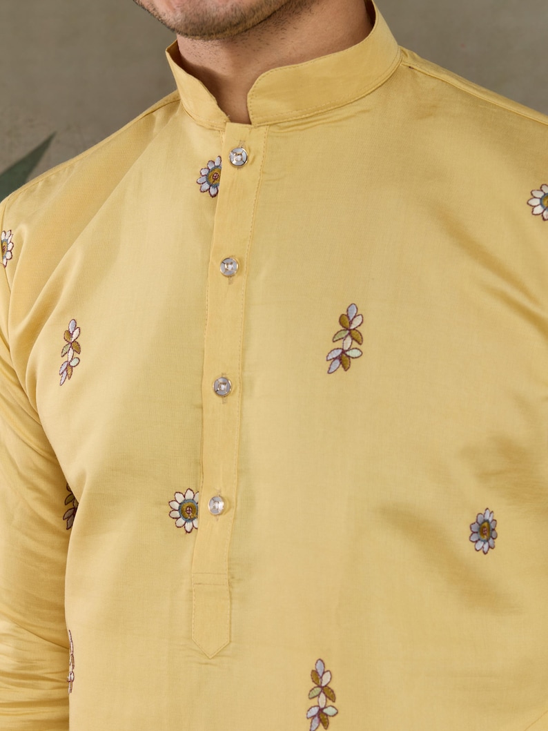 May include: A light yellow kurta shirt with a mandarin collar and floral embroidery. The shirt features clear, round buttons down the front and delicate embroidered floral patterns scattered across the fabric.