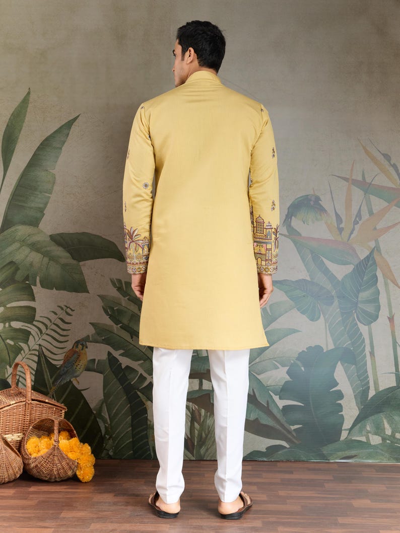 May include: A mustard yellow tunic with intricate embroidery on the sleeves, paired with white trousers. The tunic has a mandarin collar and a long, straight cut. The sleeves feature detailed patterns in shades of brown, red, and gold. The trousers are a crisp white, creating a contrasting look.