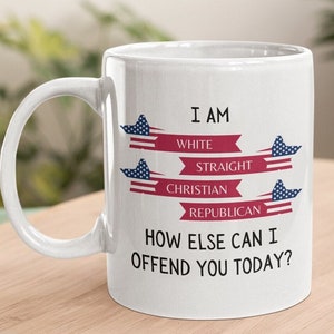 May include: White ceramic mug with a curved handle. The mug features text in black and red, including the phrases "I AM WHITE STRAIGHT CHRISTIAN REPUBLICAN" and "HOW ELSE CAN I OFFEND YOU TODAY?" Decorative elements include stylized American flags.
