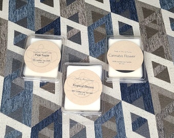 Op de afbeelding: Drie wax melts in doorzichtige plastic containers. De wax melts zijn wit en hebben labels met de namen "Pink Sugar", "Tropical Dream" en "Cannabis Flower".