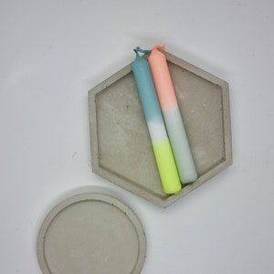 May include: Two ombre candles in a hexagonal concrete dish. The candles are teal, white, and yellow, and the other is peach, white, and yellow.