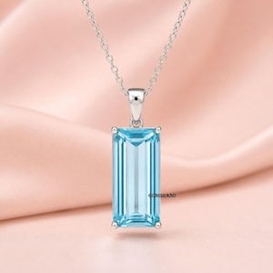 Könnte beinhalten: Eine silberfarbene Halskette mit einem rechteckigen, im Smaragdschliff gehaltenen hellblauen Edelsteinanhänger. Der Anhänger hängt an einer zarten silberfarbenen Kette. Der Text GEMBRAND ist in kleinen schwarzen Buchstaben unten rechts auf dem Stein gedruckt.