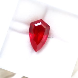 May include: A deep red gemstone with a faceted, teardrop shape. The gemstone is set against a white background.
