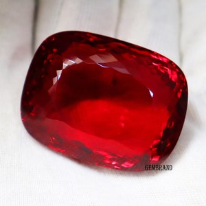 May include: A large, deep red gemstone with a cushion cut. The gemstone is faceted and has a high polish.