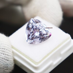 May include: A light purple gemstone with a heart shape cut. The gemstone is in a small white box with the word "GEMBRAND" printed on the side.