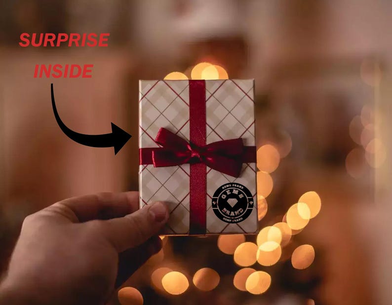 May include: A small gift box with a red ribbon and bow. The box has a white and tan plaid pattern. The words "SURPRISE INSIDE" are above the box, with an arrow pointing to it. A circular logo is on the box.