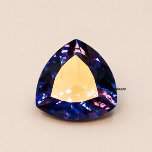 May include: A faceted gemstone with a triangular shape. The gem features a central golden-yellow section surrounded by deep blue and purple facets. The gem is set against a neutral background.