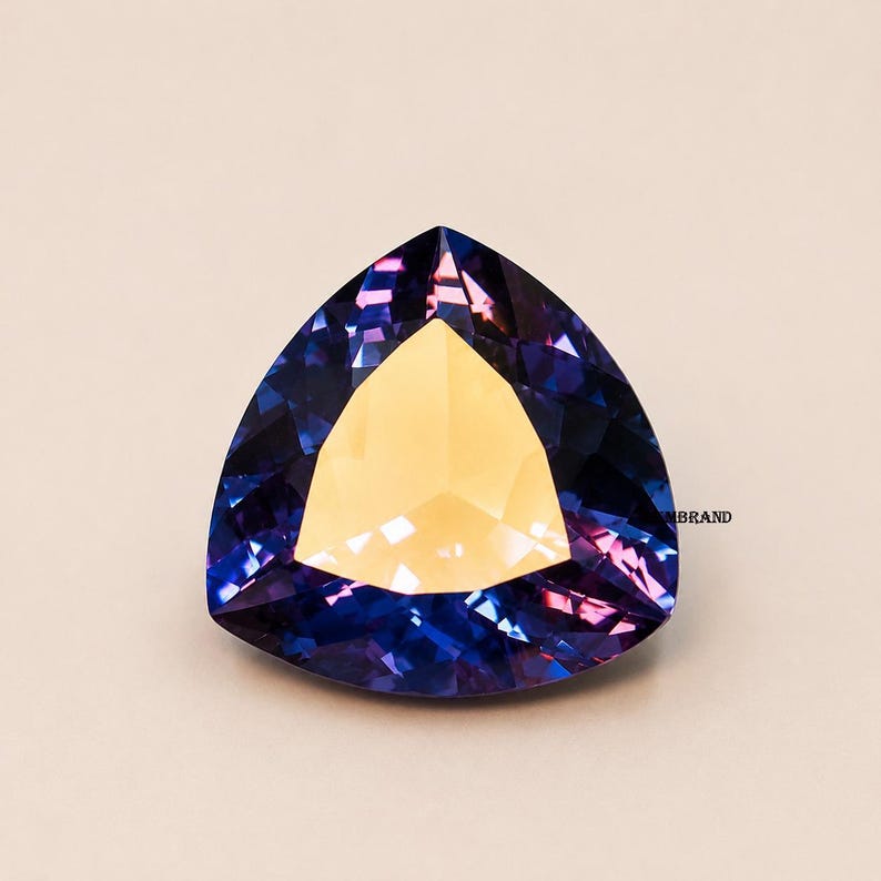 May include: A faceted gemstone with a triangular shape. The gem features a central golden-yellow section surrounded by deep blue and purple facets. The gem is set against a neutral background.