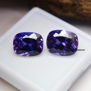 K&ouml;nnte beinhalten: Zwei kissenf&ouml;rmige violette Edelsteine, wahrscheinlich Amethyste, auf wei&szlig;em Hintergrund.