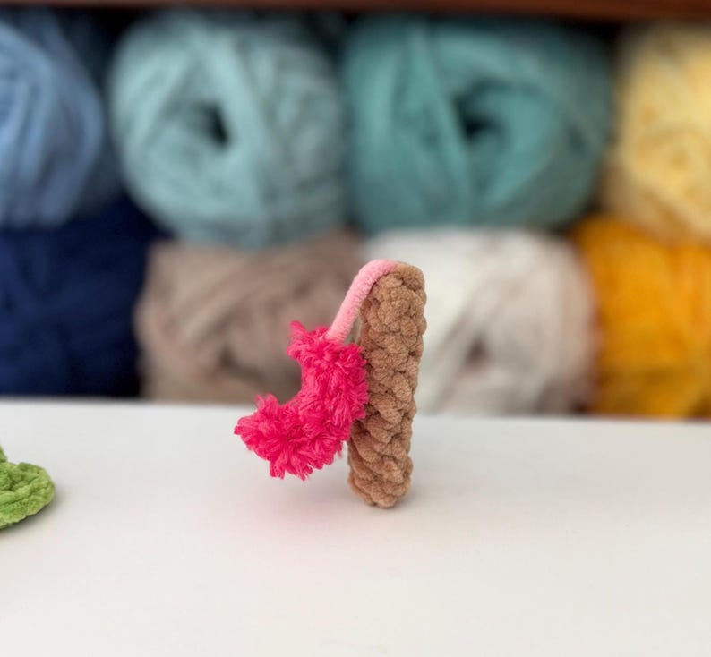 Puede incluir: Una peque&ntilde;a figura de ganchillo hecha a mano con forma de n&uacute;mero uno. El cuerpo principal est&aacute; elaborado con hilo marr&oacute;n claro con un acabado texturizado de bucles. Una pieza decorativa de color rosa brillante, difusa y texturizada est&aacute; unida al lateral con un tallo de hilo rosa fino.