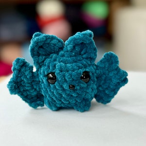 May include: A teal blue crocheted bat with black eyes. The bat is a small plush toy.