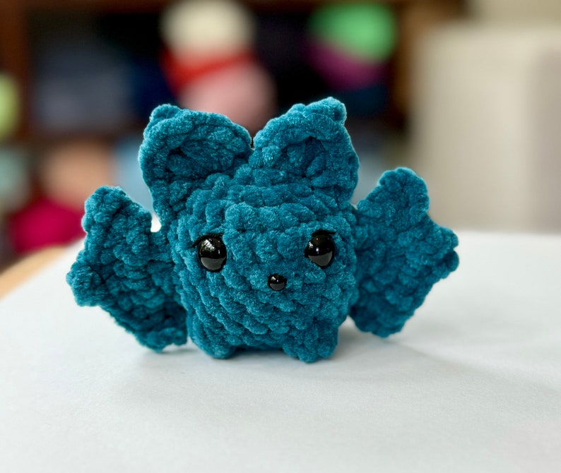 May include: A teal blue crocheted bat with black eyes. The bat is a small plush toy.