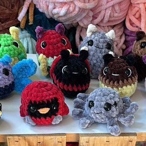 K&ouml;nnte beinhalten: Eine Sammlung von 11 geh&auml;kelten Pl&uuml;schtieren in verschiedenen Farben und Tierformen, darunter eine Biene, ein Marienk&auml;fer, ein Schmetterling, ein Oktopus und ein Vogel. Die Spielzeuge sind aus weichem, flauschigem Garn gefertigt und haben gro&szlig;e, runde Augen.