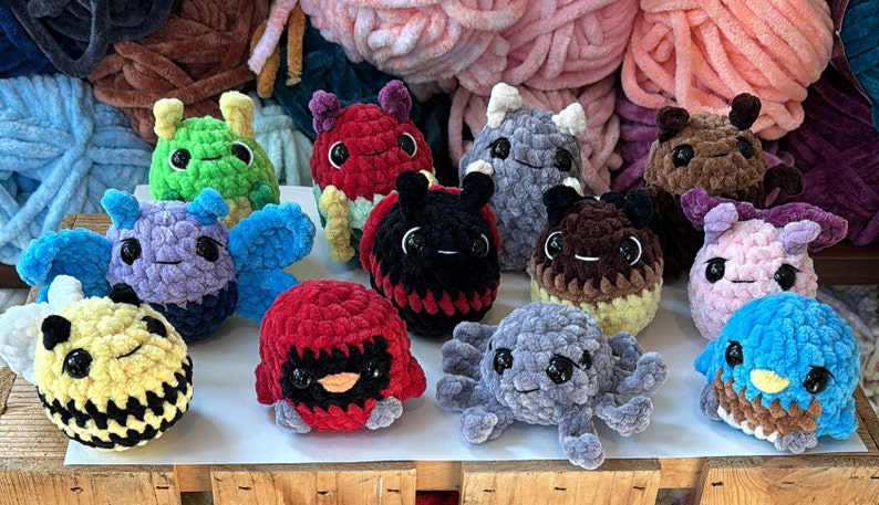 K&ouml;nnte beinhalten: Eine Sammlung von 11 geh&auml;kelten Pl&uuml;schtieren in verschiedenen Farben und Tierformen, darunter eine Biene, ein Marienk&auml;fer, ein Schmetterling, ein Oktopus und ein Vogel. Die Spielzeuge sind aus weichem, flauschigem Garn gefertigt und haben gro&szlig;e, runde Augen.