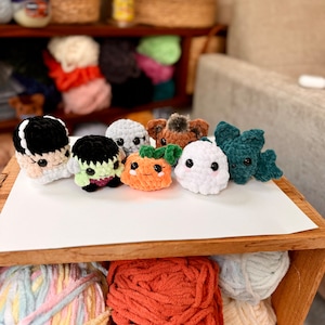 May include: A collection of eight crocheted Halloween-themed characters, including a ghost, a pumpkin, a monster, and a vampire. The characters are made with different colored yarn and have various facial expressions.