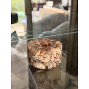 May include: A cylindrical resin paperweight or candle holder featuring a dense collection of small, multi-colored seashells embedded throughout the clear material. The object has a smooth, polished surface and a circular opening in the center.