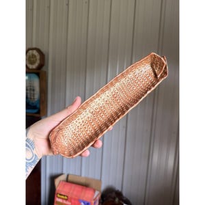 May include: A long, narrow, rectangular ceramic tray with a copper-toned metallic finish. The surface features a repeating grid of small, recessed square indentations across the entire interior, creating a textured, waffle-like appearance.