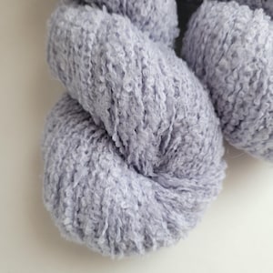 Peut inclure: Gros plan sur une pelote de laine douce, de couleur pervenche clair. La laine a un aspect texturé et bouclé, suggérant un tricot volumineux ou texturé. La laine est bien enroulée, avec des brins visibles et une texture duveteuse.