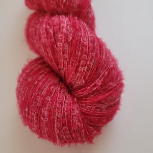 May include: A close-up of a skein of vibrant red yarn. The yarn has a textured, fluffy appearance with white flecks throughout. The yarn is tightly wound, showcasing its soft and voluminous nature, perfect for knitting or crocheting projects.