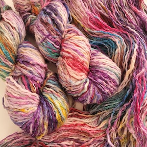 Peut inclure: Une pelote de fil coloré avec des nuances de rose, violet, bleu et blanc. Le fil est composé d'un mélange de fibres, dont la soie et le coton.