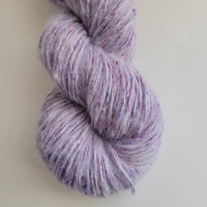 Peut inclure: Une pelote de laine lavande avec des éclats roses et bleus. La laine semble douce et duveteuse, idéale pour les projets de tricot ou de crochet. Le gros plan met en évidence la texture et les variations de couleur.