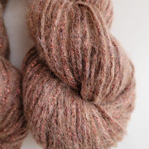 以下が含まれることがあります： 暖かくアースカラーの茶色で、銅色の光沢のある糸が織り込まれた毛糸のクローズアップ。 柔らかく、質感のある外観で、編み物や編み物プロジェクトに最適です。