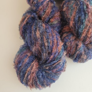 May include: A skein of yarn in shades of blue, brown, and teal. The yarn is fluffy and textured, with a fuzzy appearance.