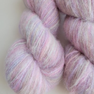Peut inclure: Une pelote de fil doux et moelleux dans des tons de rose, blanc et violet. Le fil est composé d'un mélange de fibres, créant un aspect unique et texturé.