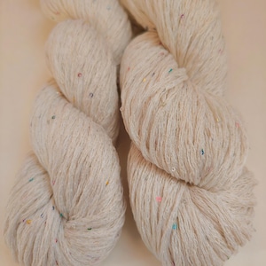 Pu&ograve; includere: Due matasse di filato color crema con macchie colorate. Il filato &egrave; ben attorcigliato, mostrando la trama delle fibre. Le macchie sono piccole e sparse, aggiungendo un tocco di colore al filato neutro. Ideale per progetti di maglia o uncinetto.