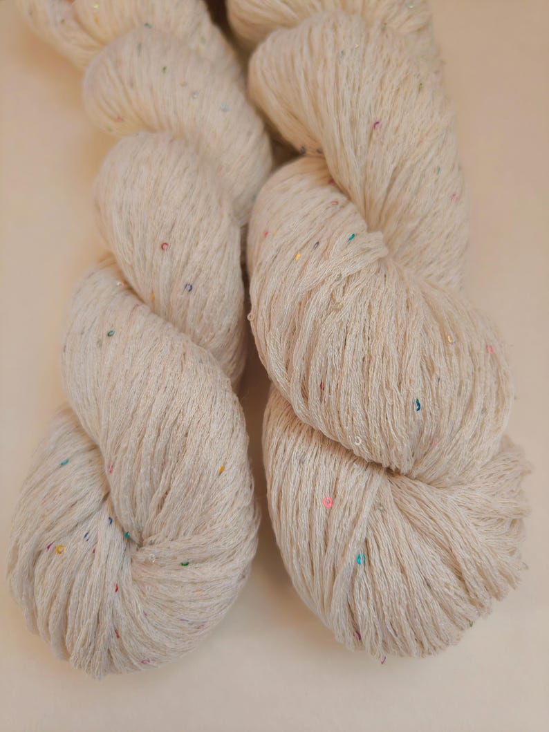 Pu&ograve; includere: Due matasse di filato color crema con macchie colorate. Il filato &egrave; ben attorcigliato, mostrando la trama delle fibre. Le macchie sono piccole e sparse, aggiungendo un tocco di colore al filato neutro. Ideale per progetti di maglia o uncinetto.