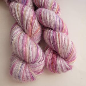 May include: Two skeins of colorful yarn in shades of pink, purple, white, and yellow. The yarn is soft and fluffy, with a slight sheen. The yarn is perfect for knitting, crocheting, or other fiber art projects.