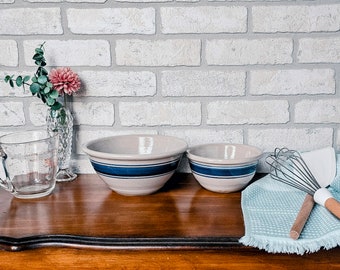 May include: Two ceramic mixing bowls with blue and white stripes on a wooden surface. A whisk and spatula are on a blue and white kitchen towel.