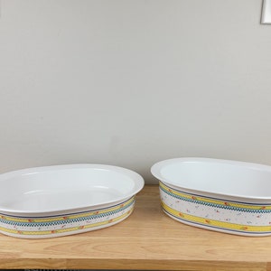 Könnte beinhalten: Zwei weiße ovale Auflaufformen mit gelben, blauen und roten Blumenmustern am Rand.