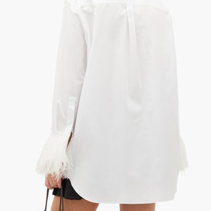 May include: White long-sleeve shirt with a classic collar and feather trim on the cuffs.