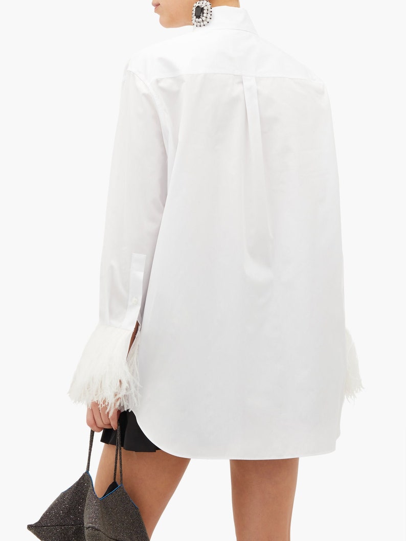 May include: White long-sleeve shirt with a classic collar and feather trim on the cuffs.