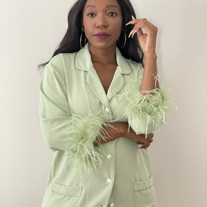 May include: A light green satin pyjama top with feather trim on the cuffs. The top has a button-up front and a collar.